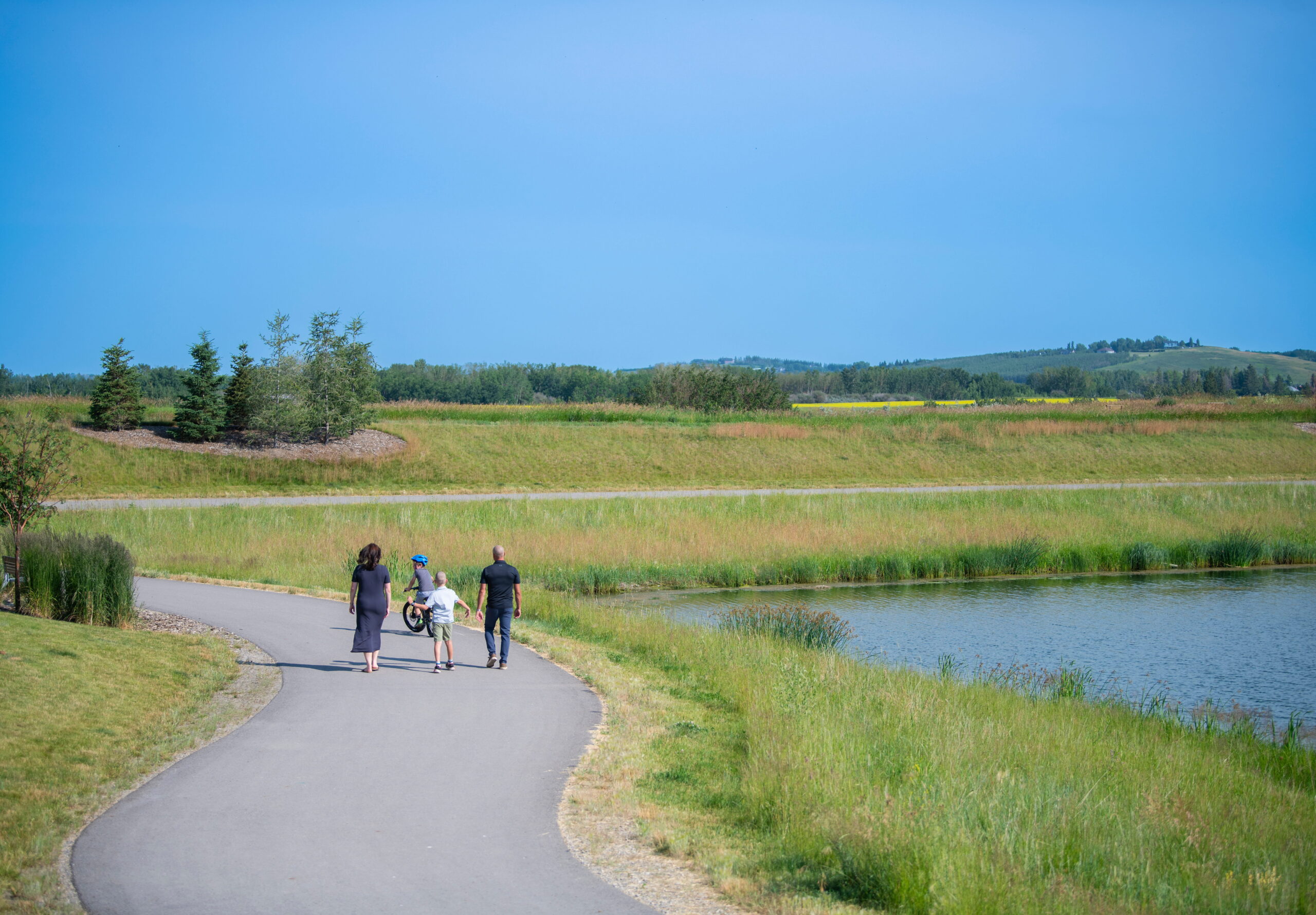 Family walking along a pathway beside the Pine Creek wetland and storm pond.